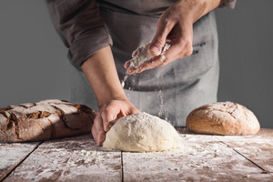 Bäcker beim Teig Kneten mit fertigen Broten daneben